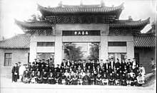 A group black and white photo of professors arranged next to a large Chinese gate
