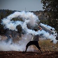 A protester uses a sling to send a tear gas grenade back towards Israeli soldiers during a Palestinian weekly protest in Ni'lin, July 2014
