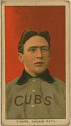 A man with brown hair wearing a grey baseball uniform with a blue collar and the word "CUBS" on his chest in front of a red background