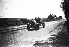 Photo d'un homme et d'un passager assis dans une voiture entourée par le public.