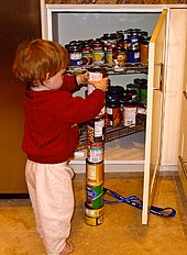 A young boy is seen stacking several colorful cans on top of each other.