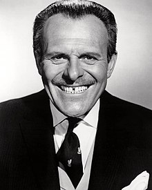 Terry-Thomas, resplendent in suit and tie, grins at the camera