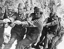 a number of men in SS uniforms and wearing fez headgear straining to pull on a rope.