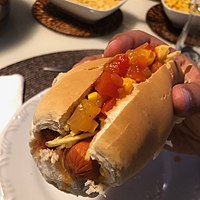 In Brazil, a cachorro-quente is served on a bread roll with a tomato-based broth, corn, and potato sticks.