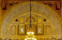 Photographie de la décoration du tympan de l'arc qui se trouve au-dessus du mihrab. Le tympan est occupé par cinq niches de différentes tailles, dont celle du milieu est la plus grande. La décoration de ce dernier inclut des carrés posés sur la pointe, des arcs à cinq lobes et des claustras garnis de verres de couleur.