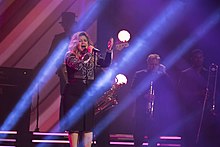 Kelly Clarkson performing with an accompanying band in a strobe-lit stage