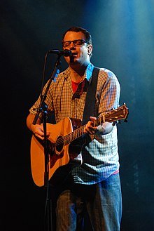 Matthew Good standing onstage, holding guitar, and singing into microphone
