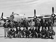 Black and white photo of 15 men in military uniforms, arrange in two rows, posing in front of a Boeing B-50D-65-BO Superfortress bomber airplane
