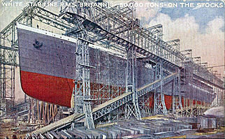 Large hull of a ship in its shipyard, painted grey above the waterline and red below