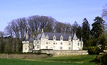 Photographie en couleurs de la façade d'un château avec un bois en arrière-plan.