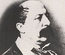 Un portrait photographique, très contrasté, d'un homme dans la force de l'âge, gégarni, portant une forte moustache, de trois-quarts face