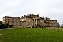 A mansion with two adjacent wings, with a gravel drive and lawn in front