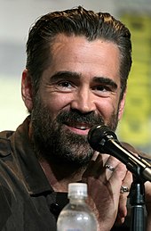 A head shot of a dark-haired, bearded man smiling behind a microphone