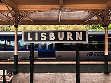 A retro-style sign reading 'Lisburn' on a platform at Lisburn railway station.