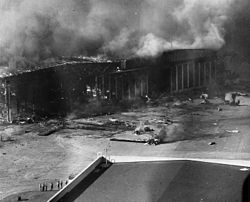 A burning hangar with destroyed planes scattered in front