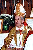 Colour photograph of Richard Williamson in white and gold Bishop's regalia standing at an altar