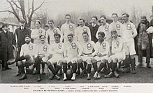 Photographie en noir et blanc. Portrait d'un groupe d'hommes habillés en blanc avec deux cercles sur le torse, alignés en rangs assis ou debout.