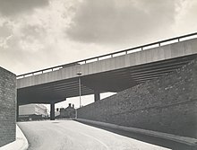 View of a ramp leading up to the Moat Street roundabout car park with brick walls on both sides, the ring road flyover passing from right to left over the car park