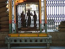 Four black statuettes housed in a wooden vehicle-like structure