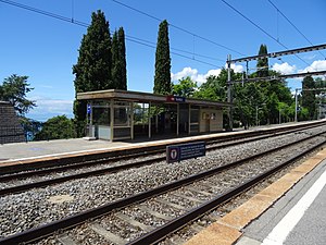 Double-track railway next to a lake with canopy-covered shelter on platform