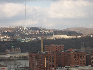 Spring Hill (background, with radio mast), as seen from Frank Curto Park. The Cork Factory lofts in the Strip District and Troy Hill are located in the foreground.