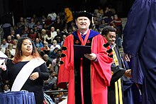 Man in red robe regalia stands on stage