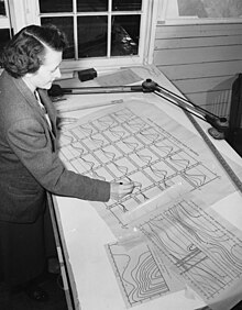 Margaret King Robinson, a white woman with dark hair in a side part, standing at a desk with large oceanographic data charts