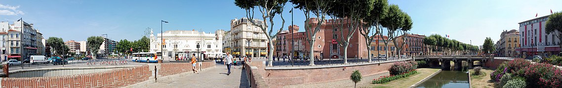 Vue du centre-ville de Perpignan. À gauche, la place de la Résistance, lieu de jonction du boulevard Georges-Clemenceau et du boulevard Wilson. Au centre droit, le Castillet (El Castellet). La rivière la Basse, petit affluent du fleuve côtier la Têt est longée par le quai Sadi-Carnot (à gauche) où se trouvent la préfecture et le conseil départemental, et à droite le quai Vauban et ses commerces.