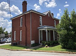 A two-story red brick building with a one-story porch, a hipped roof and three chimneys.