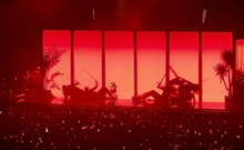 SZA in front of a red stage screen, with silhouettes of defeated fighters in the background