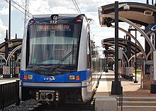 A blue and gray train stopped at a side platform station with station black and gray station canopies visible.