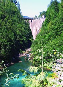 An arch dam straddles a narrow, forested canyon above a tumbling river