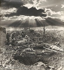 Une photographie d'un paysage boueux et déchiqueté avec un blockhaus en béton et des hommes couchés sur le sol.