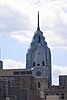 A skyscraper tower behind a building with a statue on top