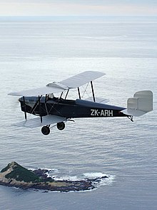 Photograph of a Spartan Three Seater flying over water with a point of land in the background