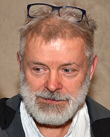 close-up of Vladimír Kokolia wearing his glasses atop his head, looking down and left of camera