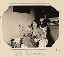 Photo of Vita Sackville-West in armchair at Virginia's home at Monk's House, smoking and with dog on her lap
