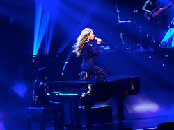 A woman sits upon a piano whilst singing