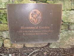 Metal, square plaque mounted on a stone structure with the words "Bicentennial Garden, a gift to the City & Citizens of Greensboro, by Greensboro Beautiful, Inc.