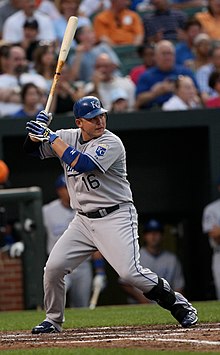 A man in a gray baseball uniform and blue batting helmet prepares to swing in a right-handed batting stance.