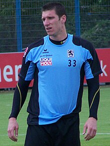A brown-haired caucasian male in a blue and black training kit.