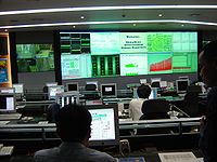 Three people working on computers in a control room