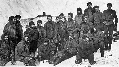 A group of men sitting closely packed together in heavy winter clothes and hats. Snow and ice surrounds them.
