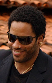 Lenny Kravitz smiling in a tuxedo and black sunglasses.