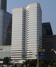 Two attached concrete and glass office towers, one with an irregular shape. Both have uniform horizontal bands of windows alternating with the concrete.