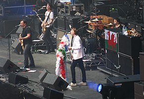Manic Street Preachers in 2010. From left to right: James Dean Bradfield, touring member Wayne Murray, Nicky Wire and Sean Moore; the open microphone on the far right is a traditional memorial to former member Richey Edwards, who disappeared in 1995.