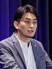 A Japanese man speaking at a podium