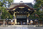 Frontal view of a black wooden gate with a large dominating roof with an undulating gable and golden metal decorations.