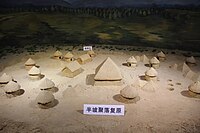 A diorama of a Neolithic village with many small circular and rectangular houses surrounding a larger square structure.