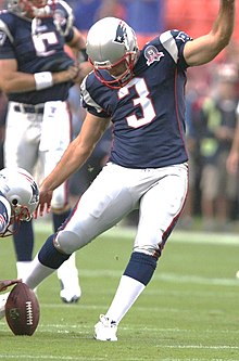 Stephen Gostkowski in a New England Patriots uniform and helmet about to kick a football.